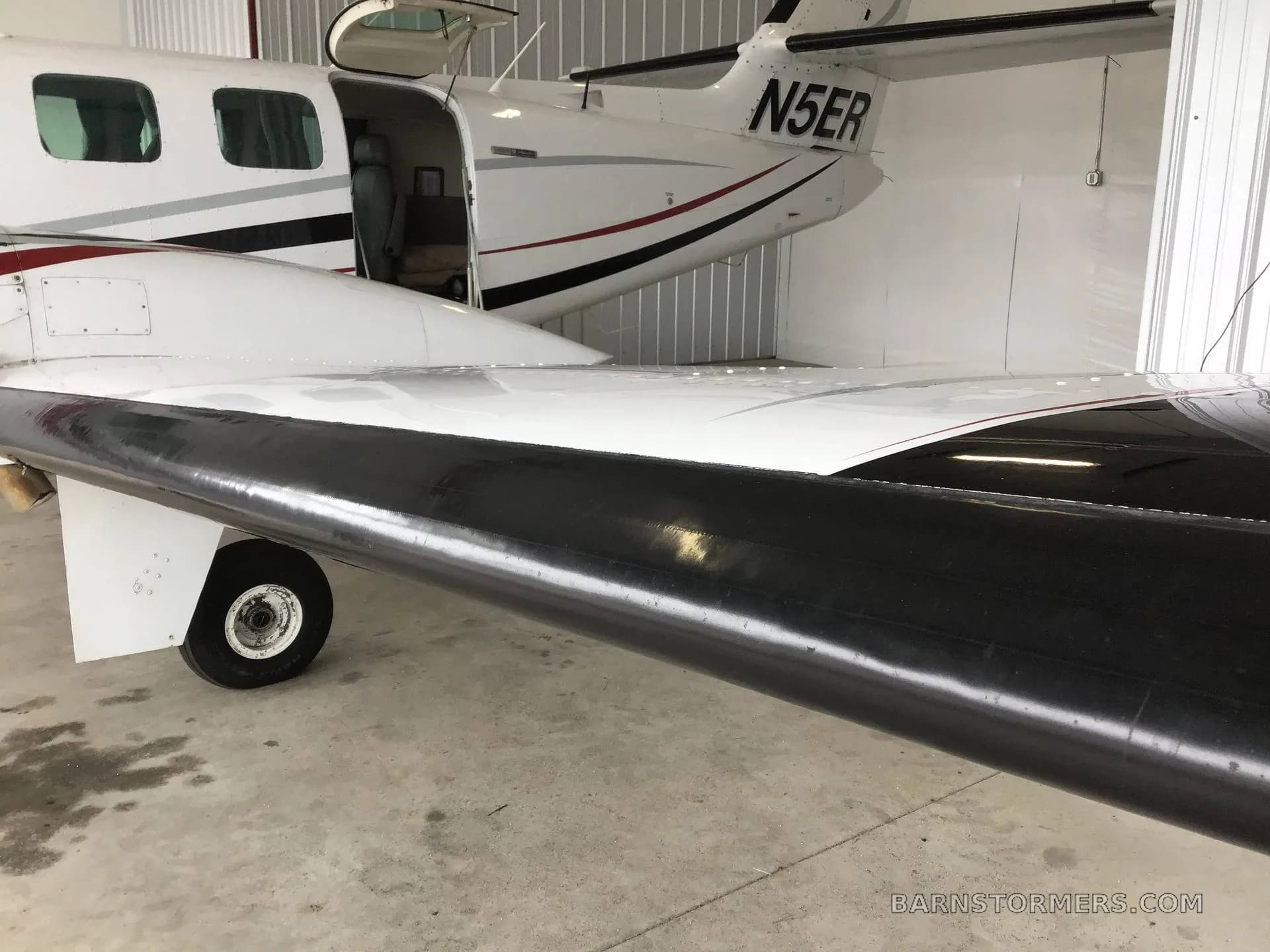 A close-up view of the rear fuselage, tail, and black wing of a white twin-engine aircraft with registration N5ER, parked in a hangar.