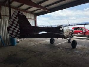 Side view of a red Cubcrafters aircraft with a checkered tail in a hangar.