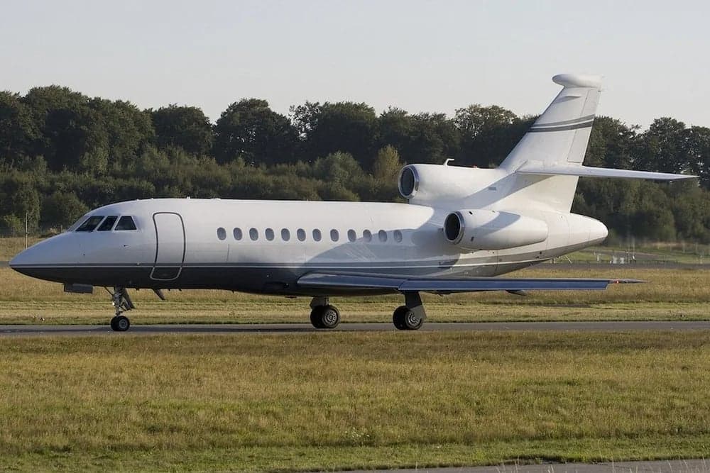 Side view of a white and gray Falcon jet on the ground.