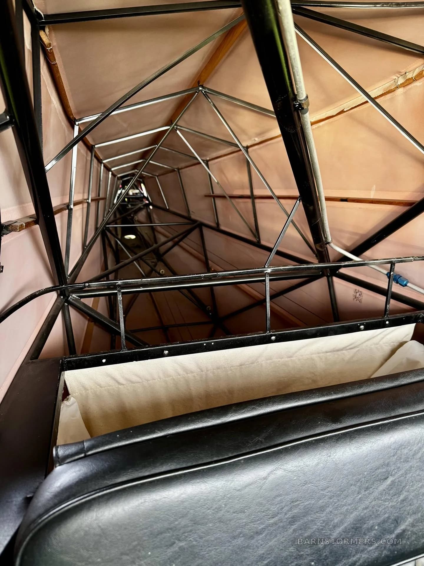 An upward view into the fabric-lined fuselage of a Piper Cub, revealing the internal metal framework and structure.