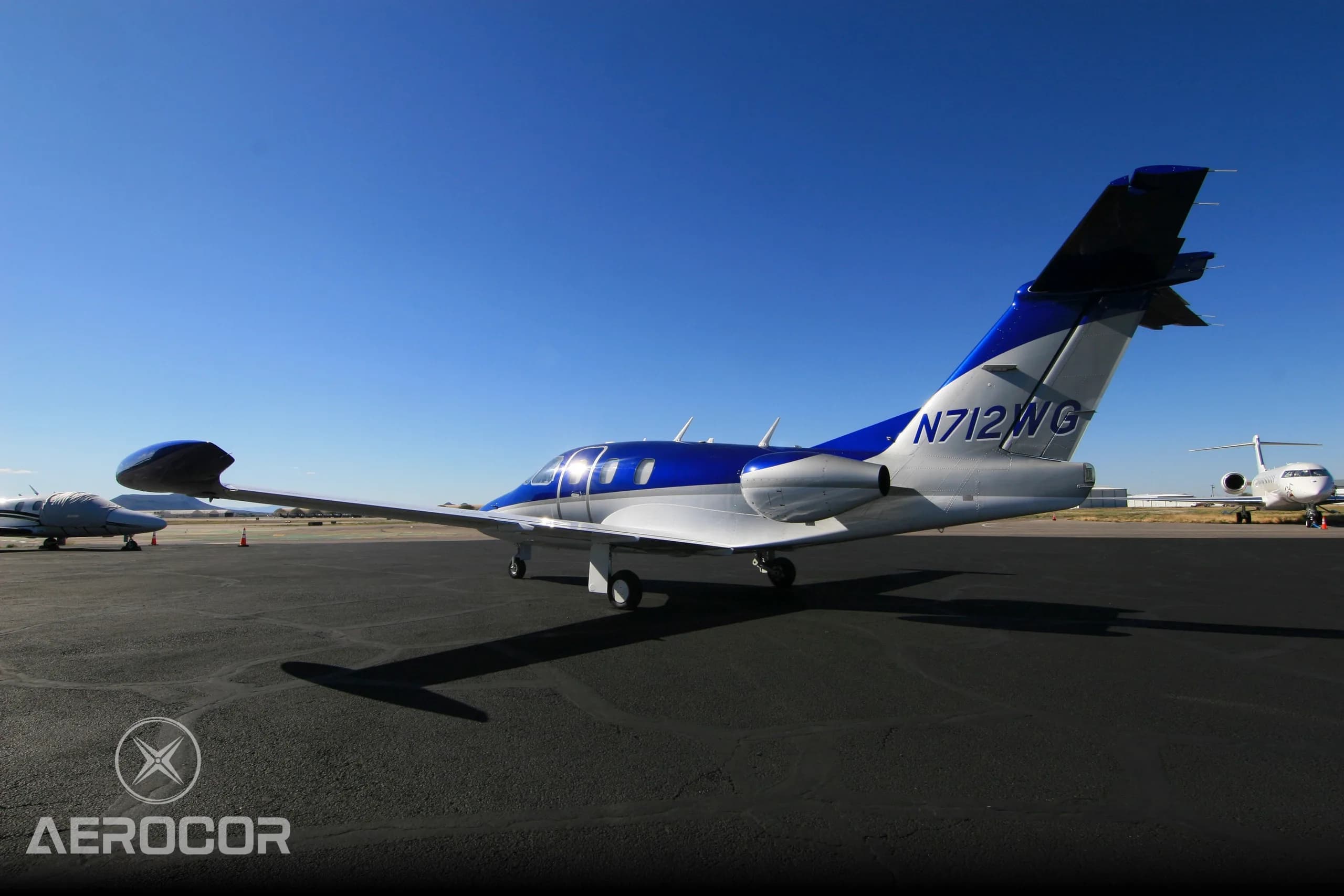 A rear-side view of the blue and white Eclipse 500/550 jet, N712WG, on an airport tarmac.