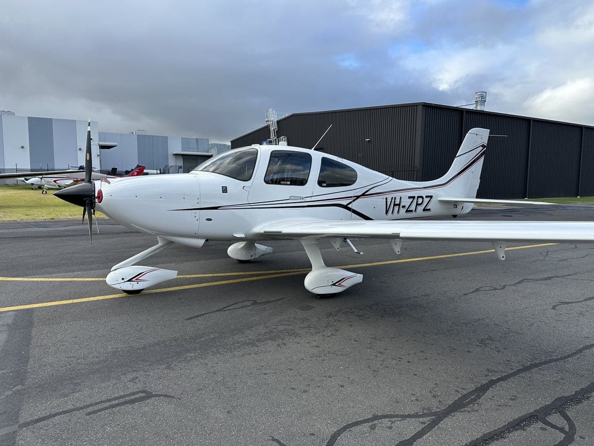 A white Cirrus aircraft with black accents parked on the tarmac.
