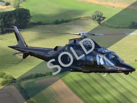 A black AgustaWestland AW109 helicopter in flight over a rural landscape, with a 'SOLD' overlay.