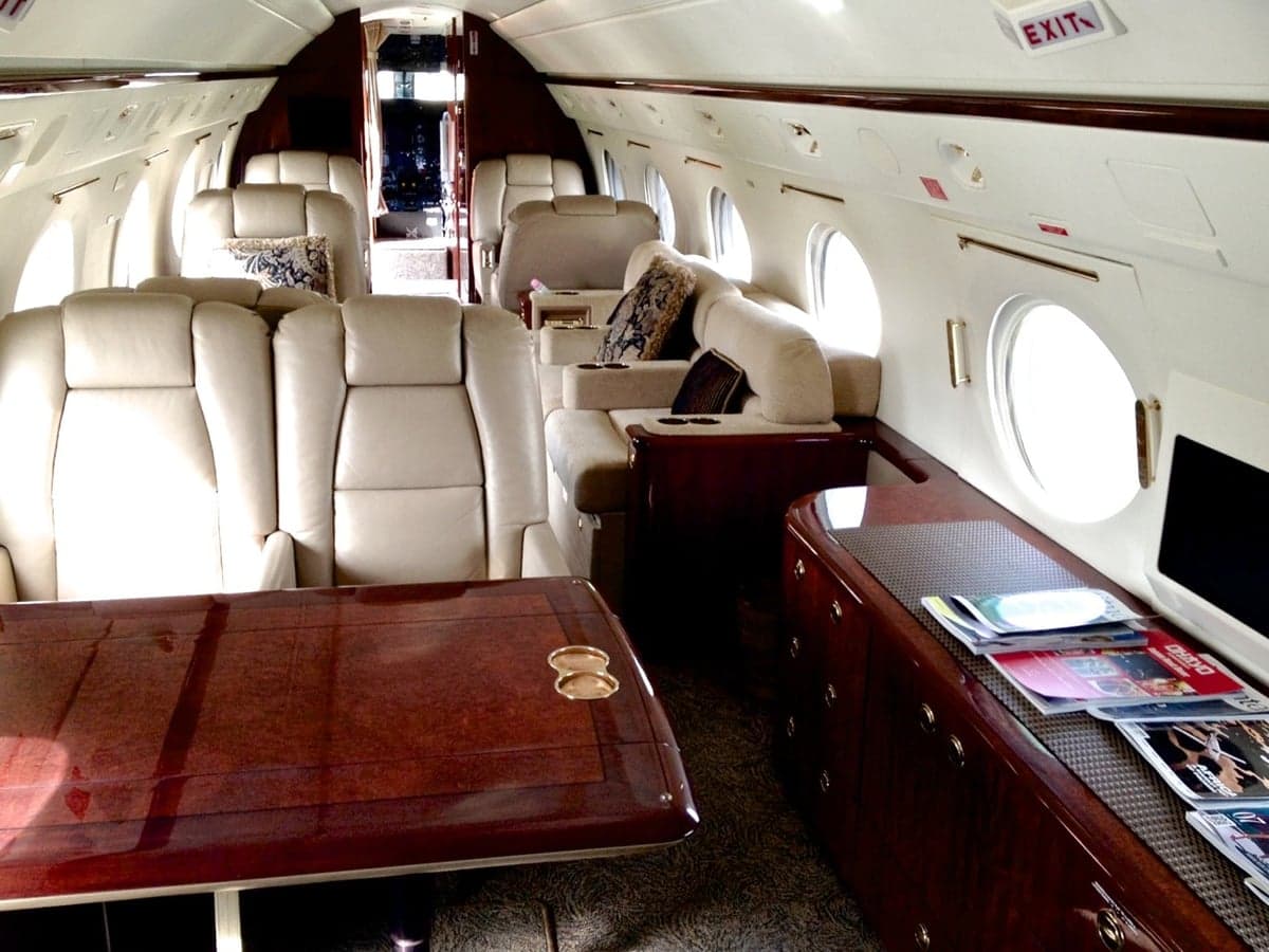 Interior of the aircraft featuring leather seats, a wooden table, and a wooden cabinet with magazines.