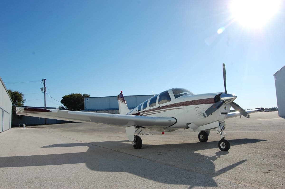 A Beechcraft Bonanza sits on the tarmac in the sun.