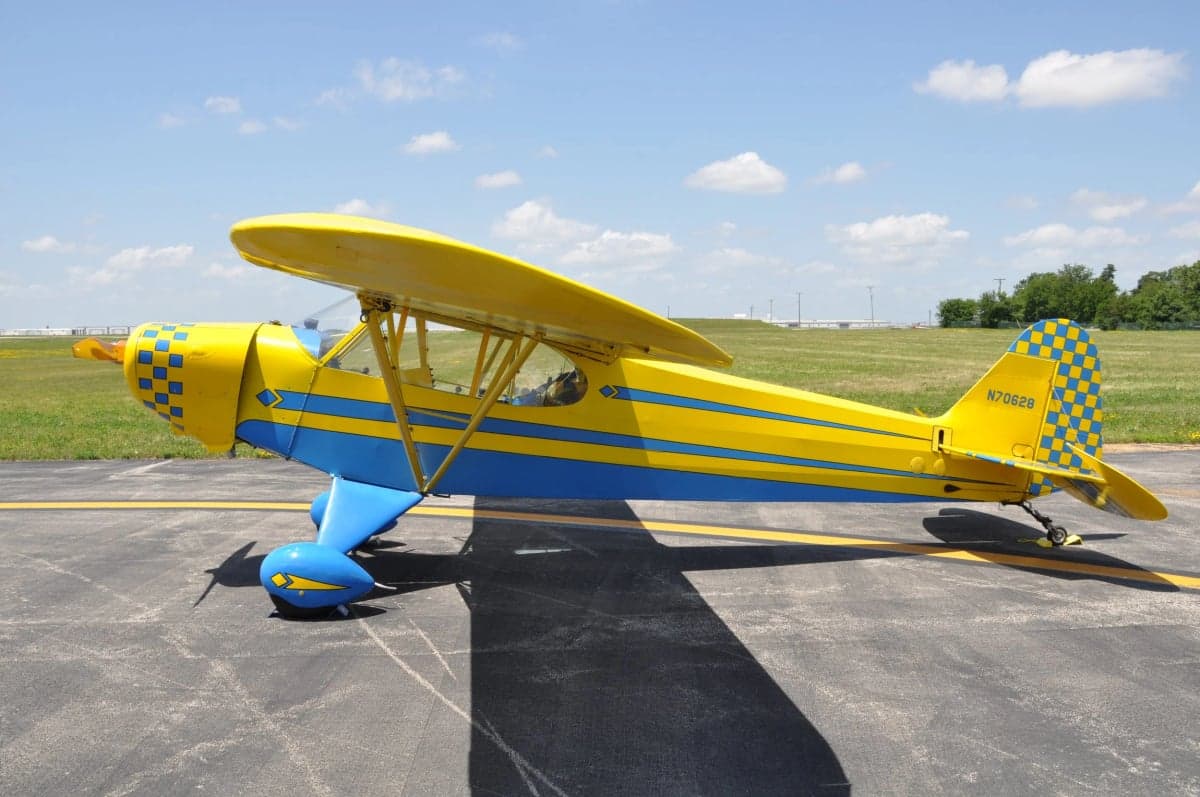 A yellow and blue Piper Cub aircraft on the tarmac.