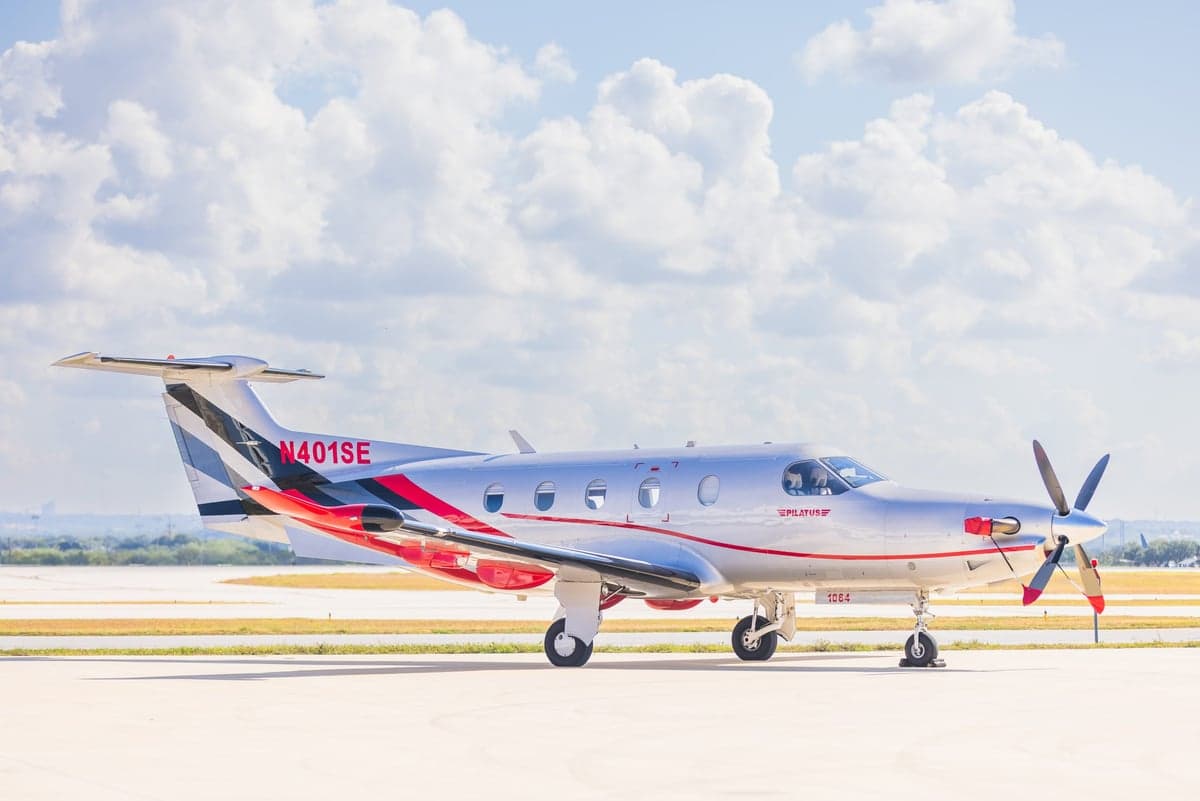A Pilatus PC-12NG aircraft on the tarmac with a silver and red paint scheme, side view.