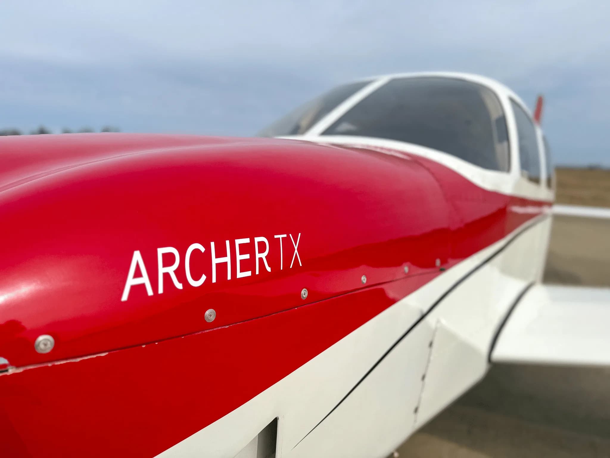 A close-up view of the red cowling and white fuselage of a Piper Archer TX aircraft.