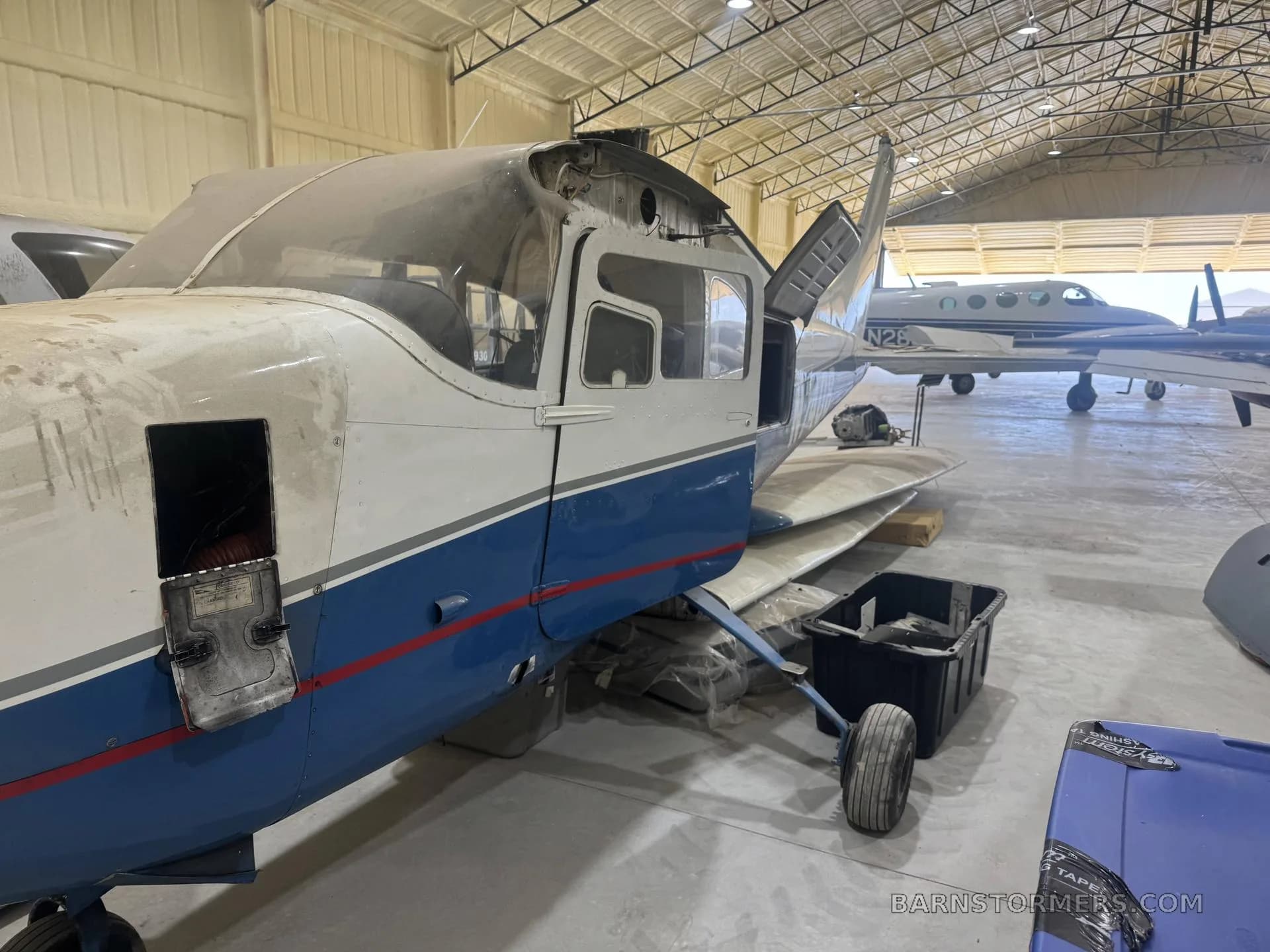 A partially disassembled blue and white single-engine aircraft (N740B) with its cowling removed, inside a hangar.
