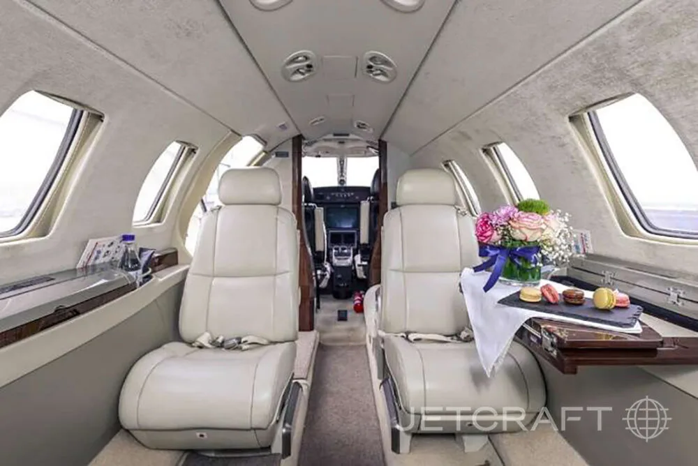 The luxurious interior cabin of a private jet with light-colored leather seats and a table with flowers and macarons.
