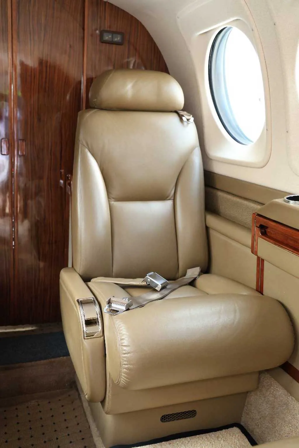 A close-up of a single tan leather passenger seat inside an aircraft cabin.
