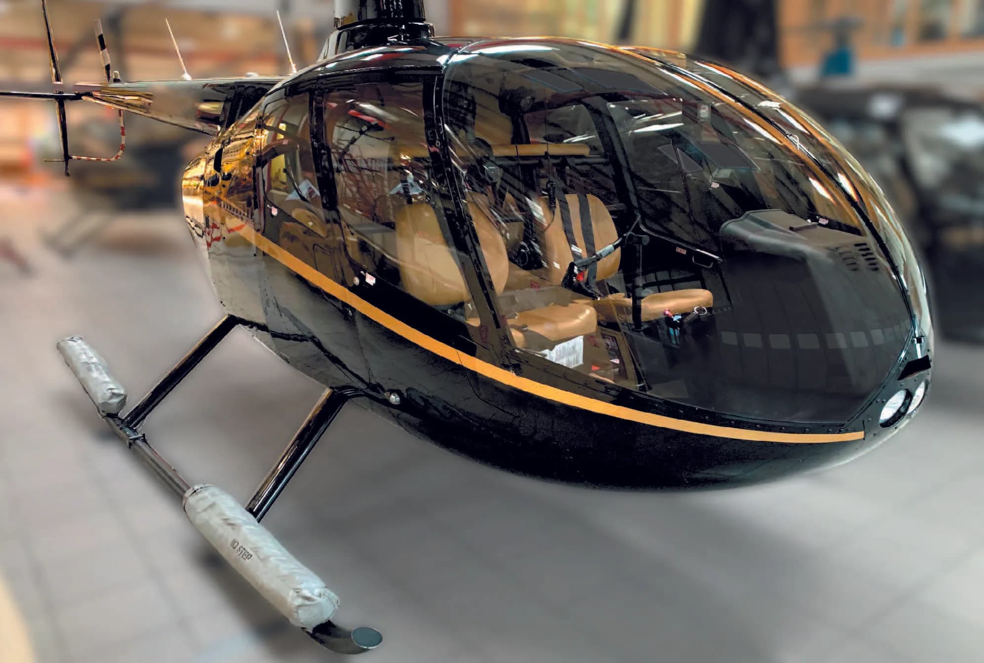 A close-up view of the front of a black Robinson R66 Turbine helicopter with gold stripes and floats, inside a hangar.