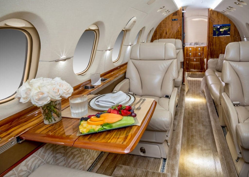 View of the aircraft's interior with leather seats, wood trim, and tables set for dining.