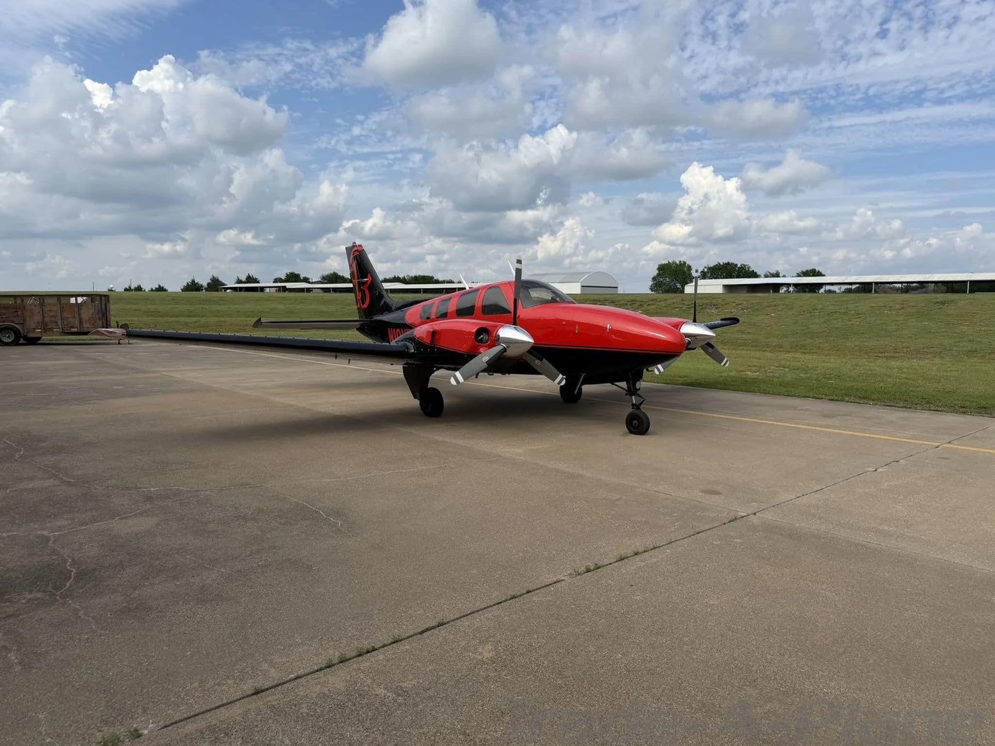 A red and black twin-engine propeller aircraft, N10NF, parked on an airfield tarmac under a cloudy sky.