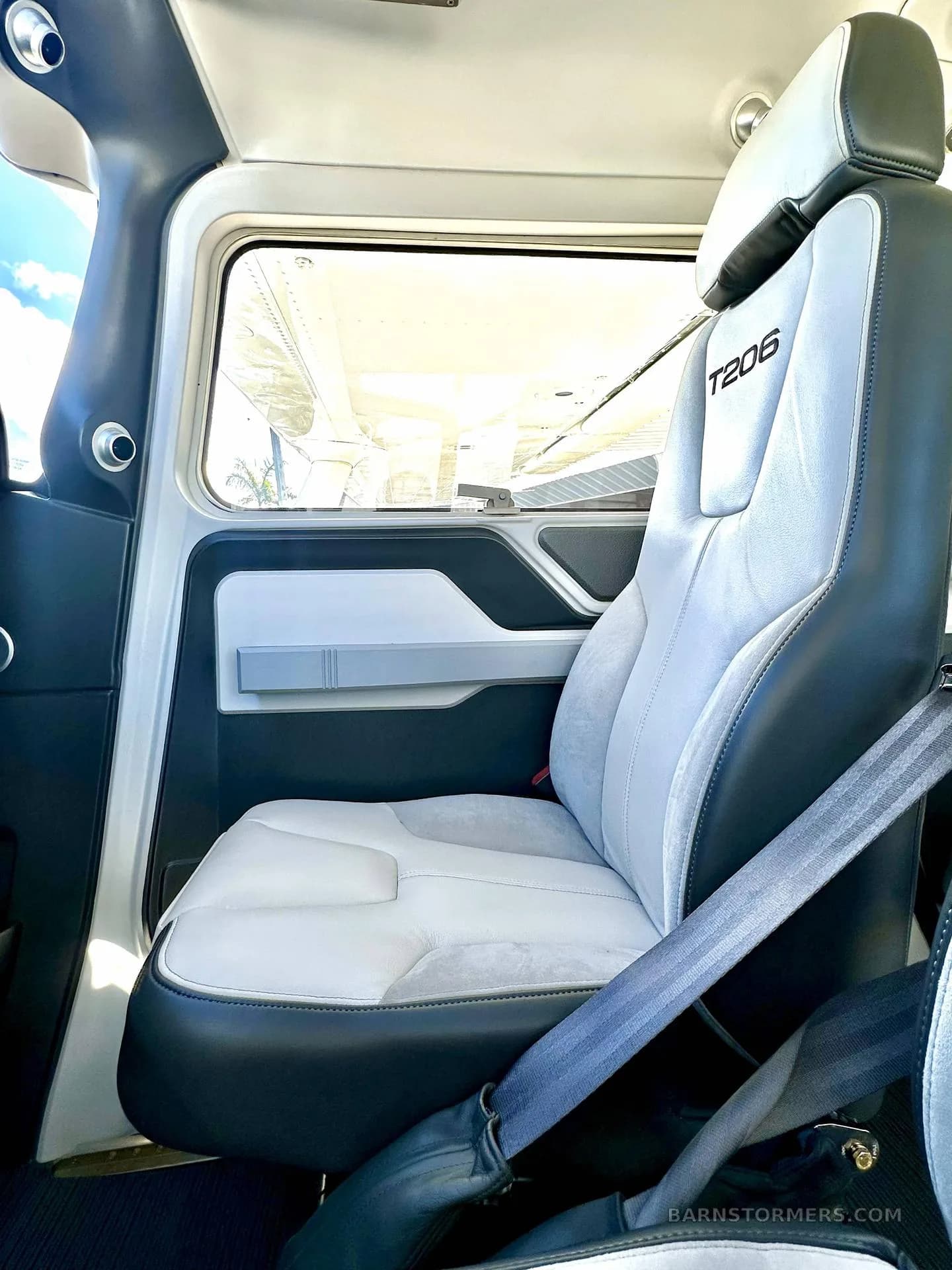 A light gray and black leather passenger seat with "T206" embroidered on the headrest is seen inside a Cessna T206 cabin.