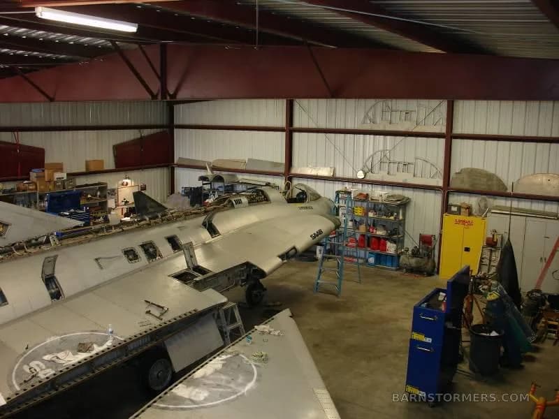 An overhead view of a disassembled Saab Draken aircraft undergoing maintenance in a hangar.