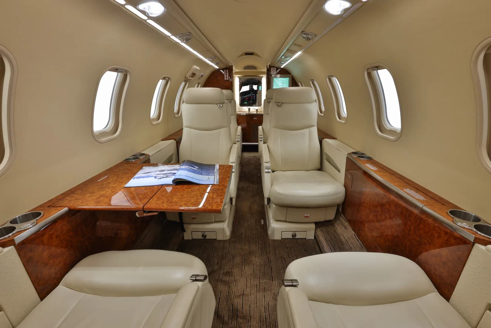 View of the cabin interior with cream-colored seats and wood table.