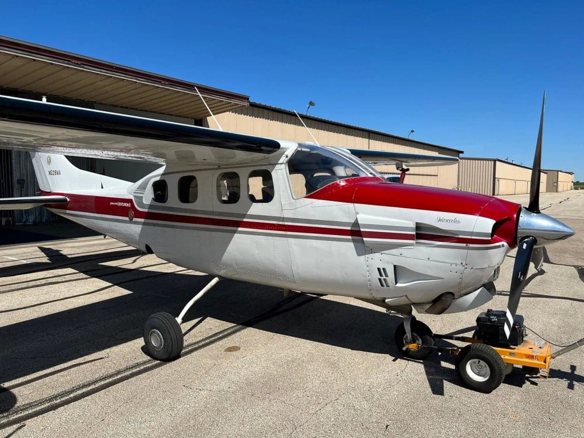 Side view of a red and white Cessna Centurion II aircraft, registration N528WA, parked on an airfield with a tug attached.