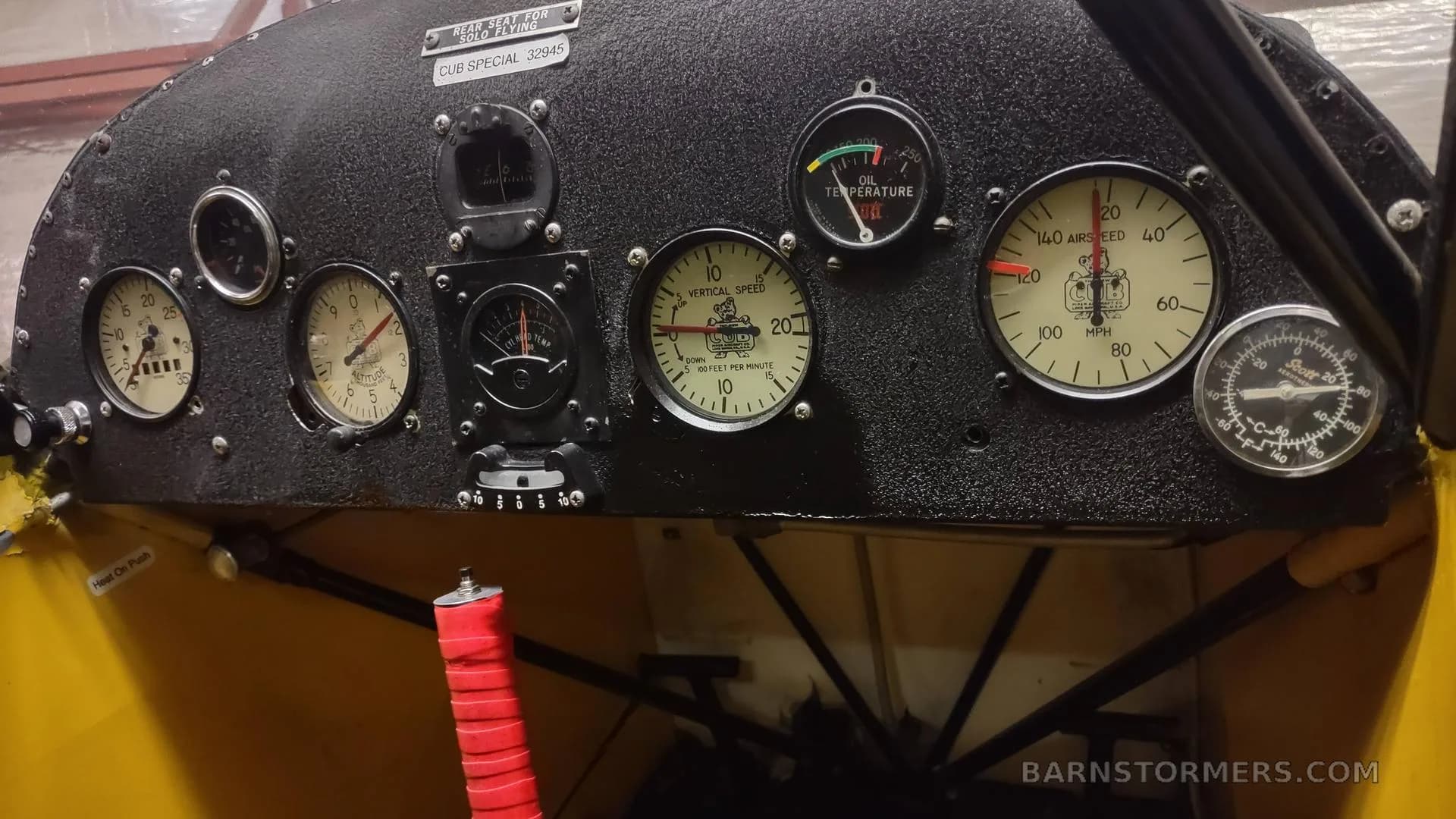 The main instrument panel of a yellow aircraft, showing various gauges and a red-wrapped control stick.