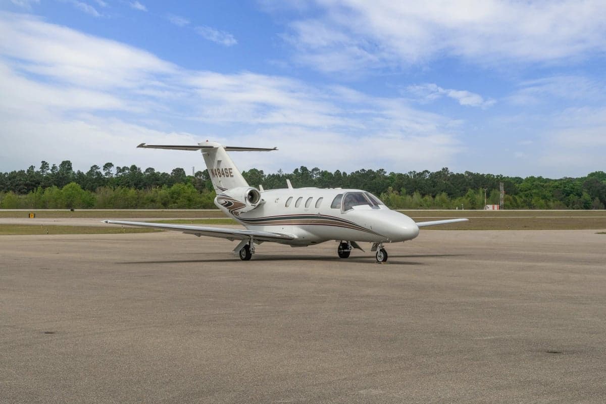 A Cessna Citation CJ1 parked on the tarmac with trees in the background.