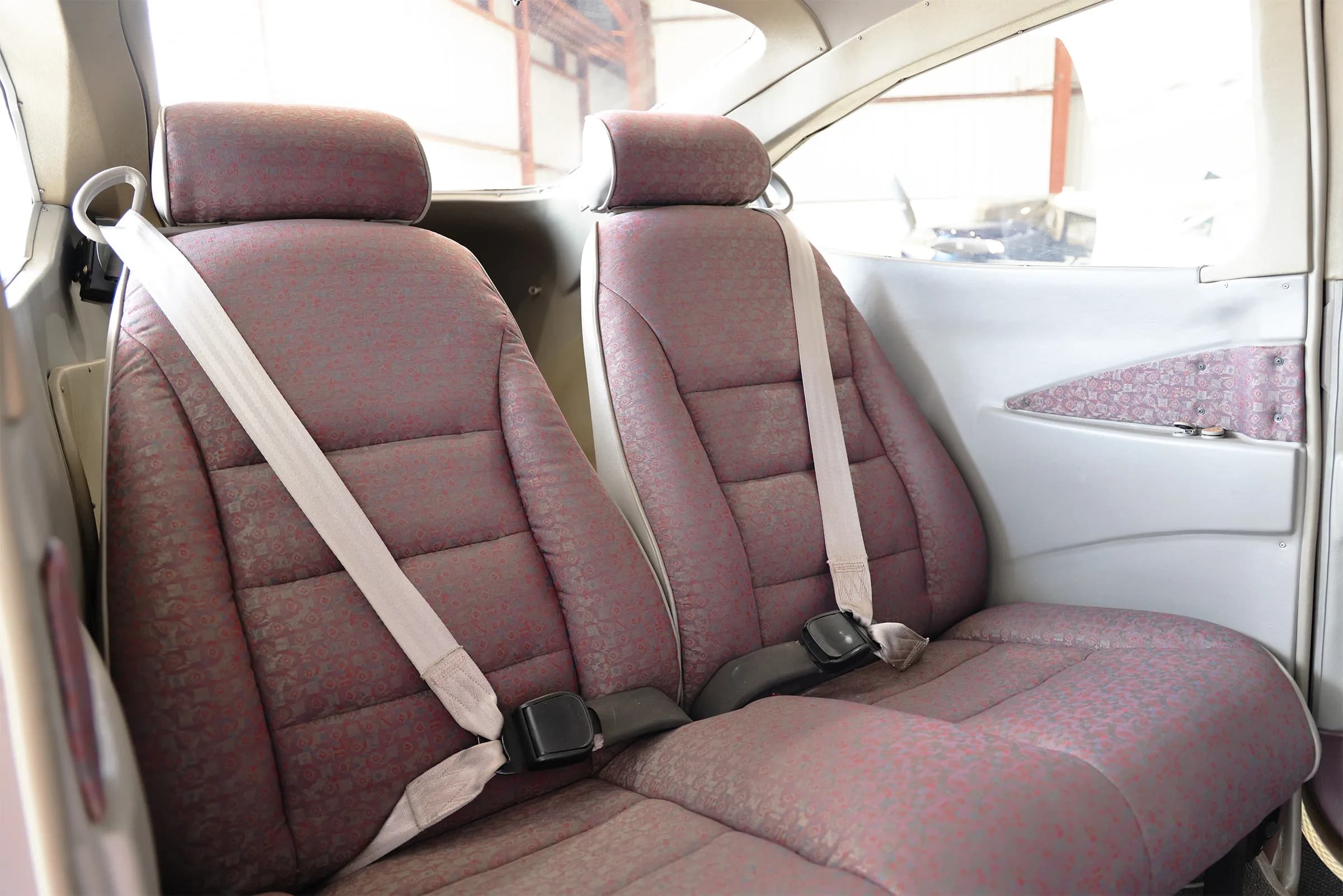 Two red patterned fabric seats with seatbelts in the aircraft cabin.