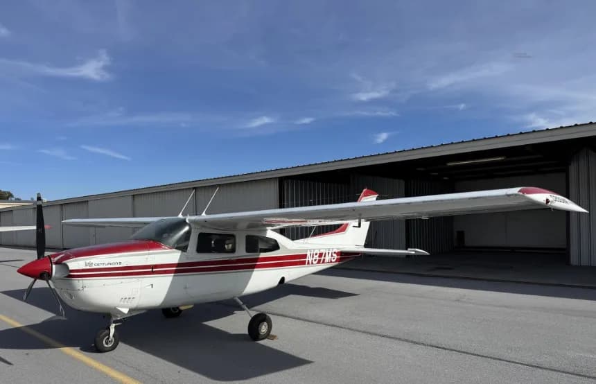 A front-left view of a white and red Cessna 182 Skylane (N87MS) parked on an airport tarmac.