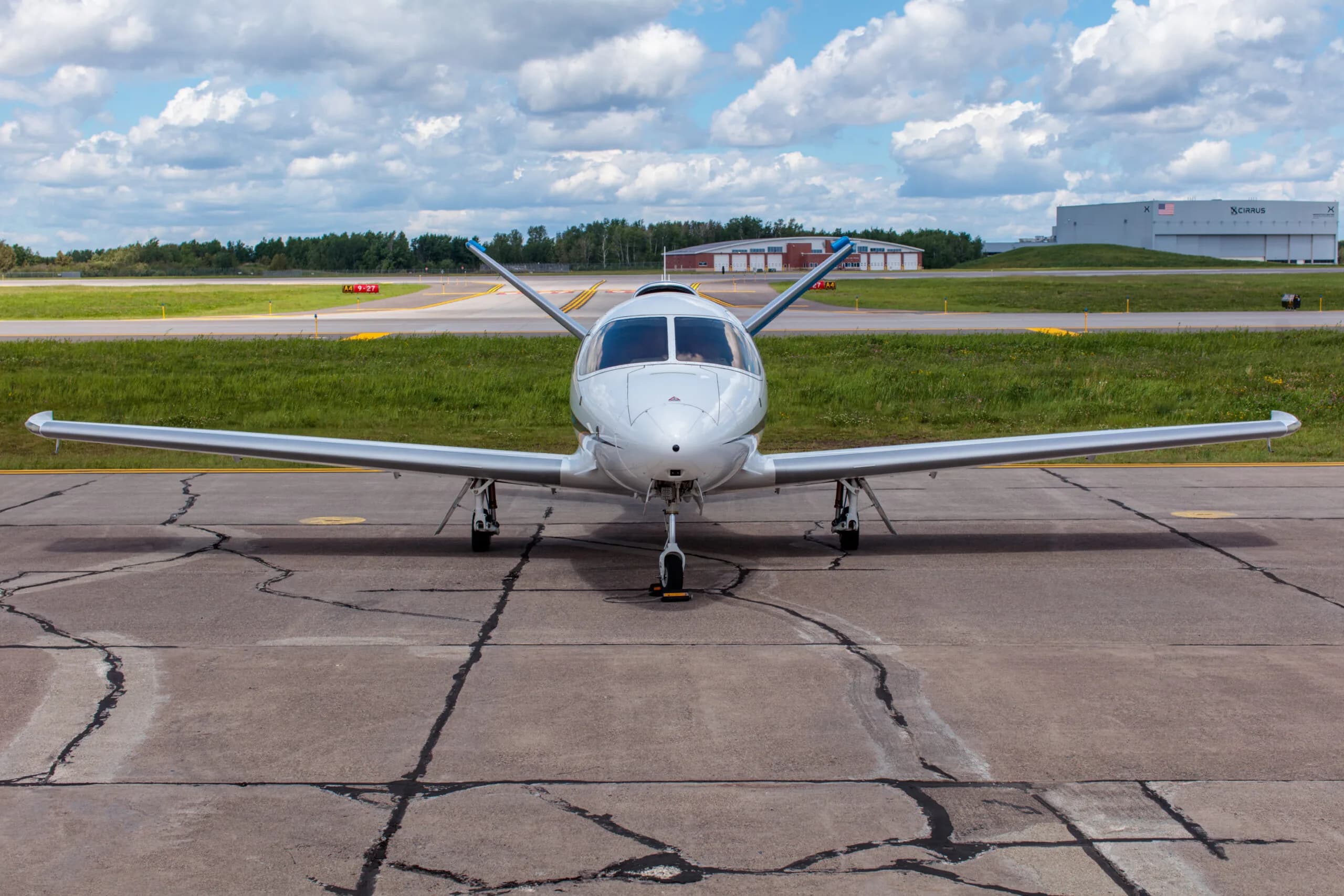 Front view of a white Cirrus Vision Jet (N218HP) parked on a tarmac with a hangar in the distance.