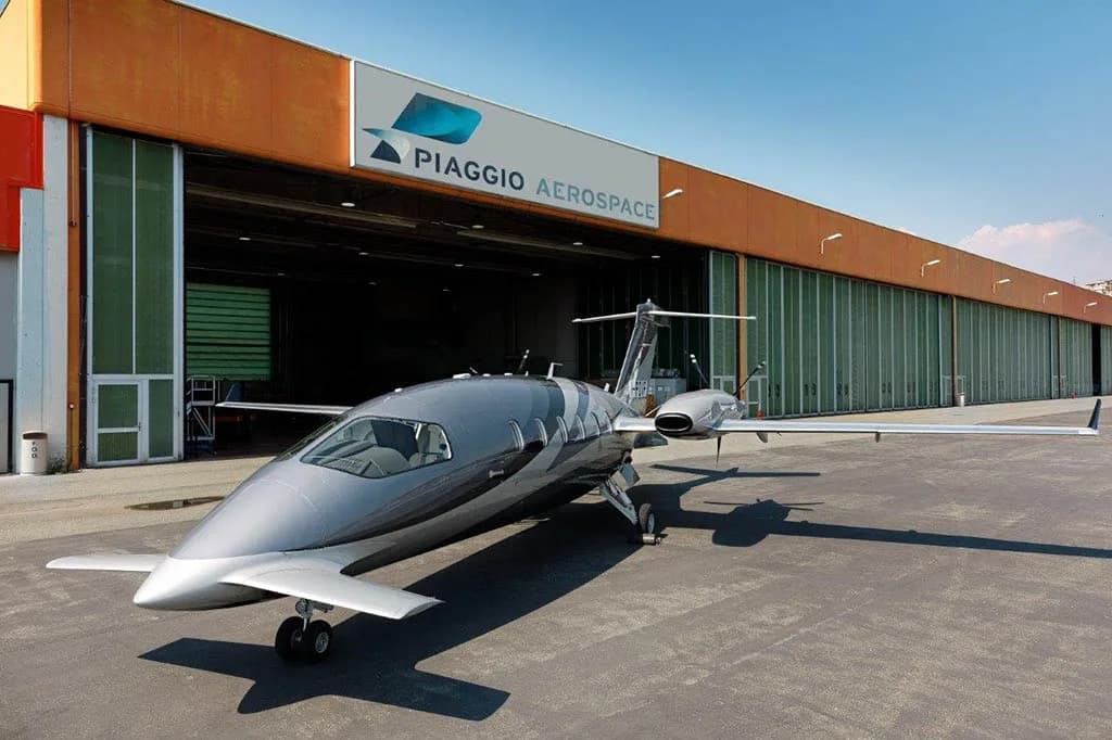 A silver Piaggio P.180 Avanti aircraft parked in front of a Piaggio Aerospace hangar.