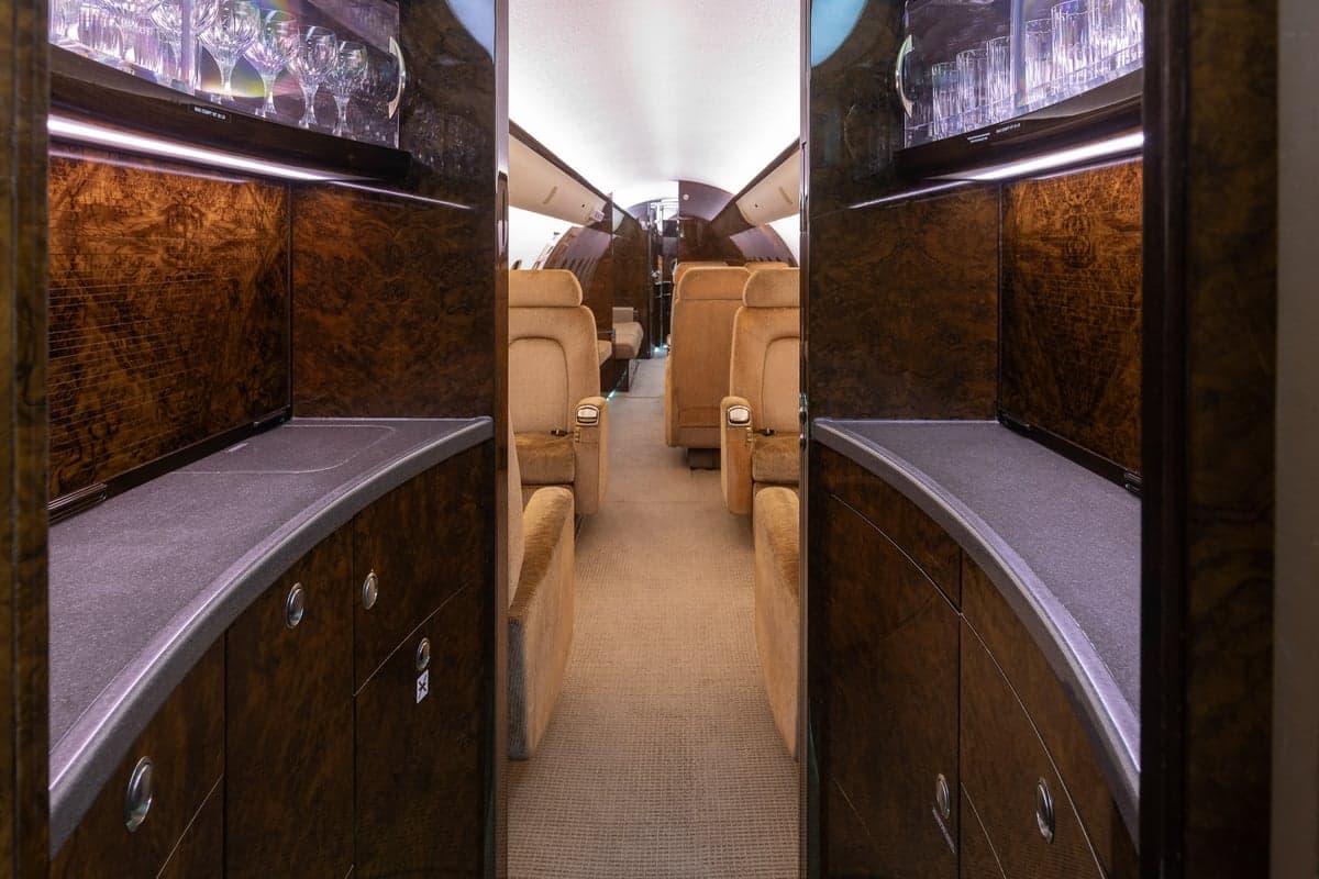 The interior of a Bombardier Global Express aircraft with tan leather seats and a bar area.
