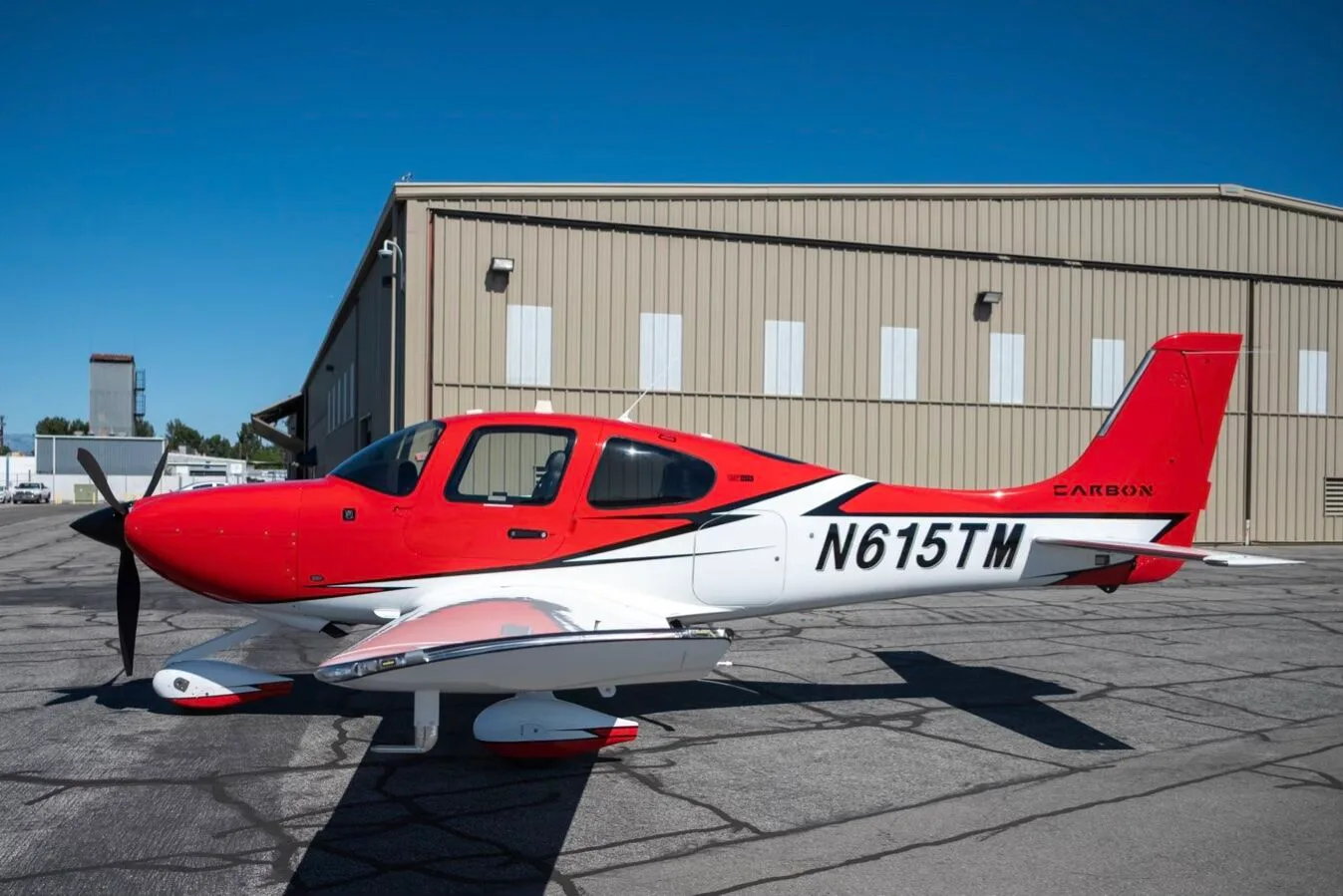 Side view of a red and white N615TM aircraft with its doors closed, parked in front of a hangar.