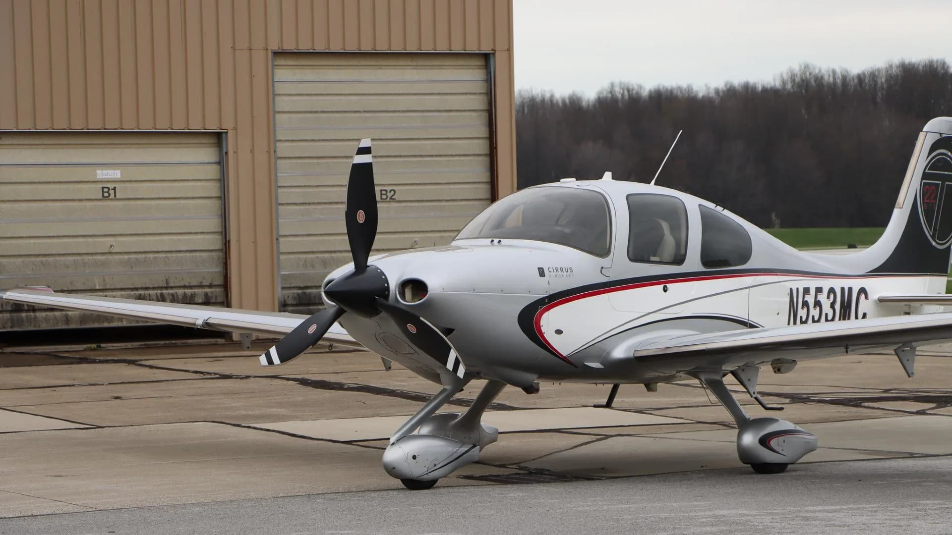 A close-up front-left view of the Cirrus SR22 N553MC, showing the propeller and nose, parked next to a hangar.