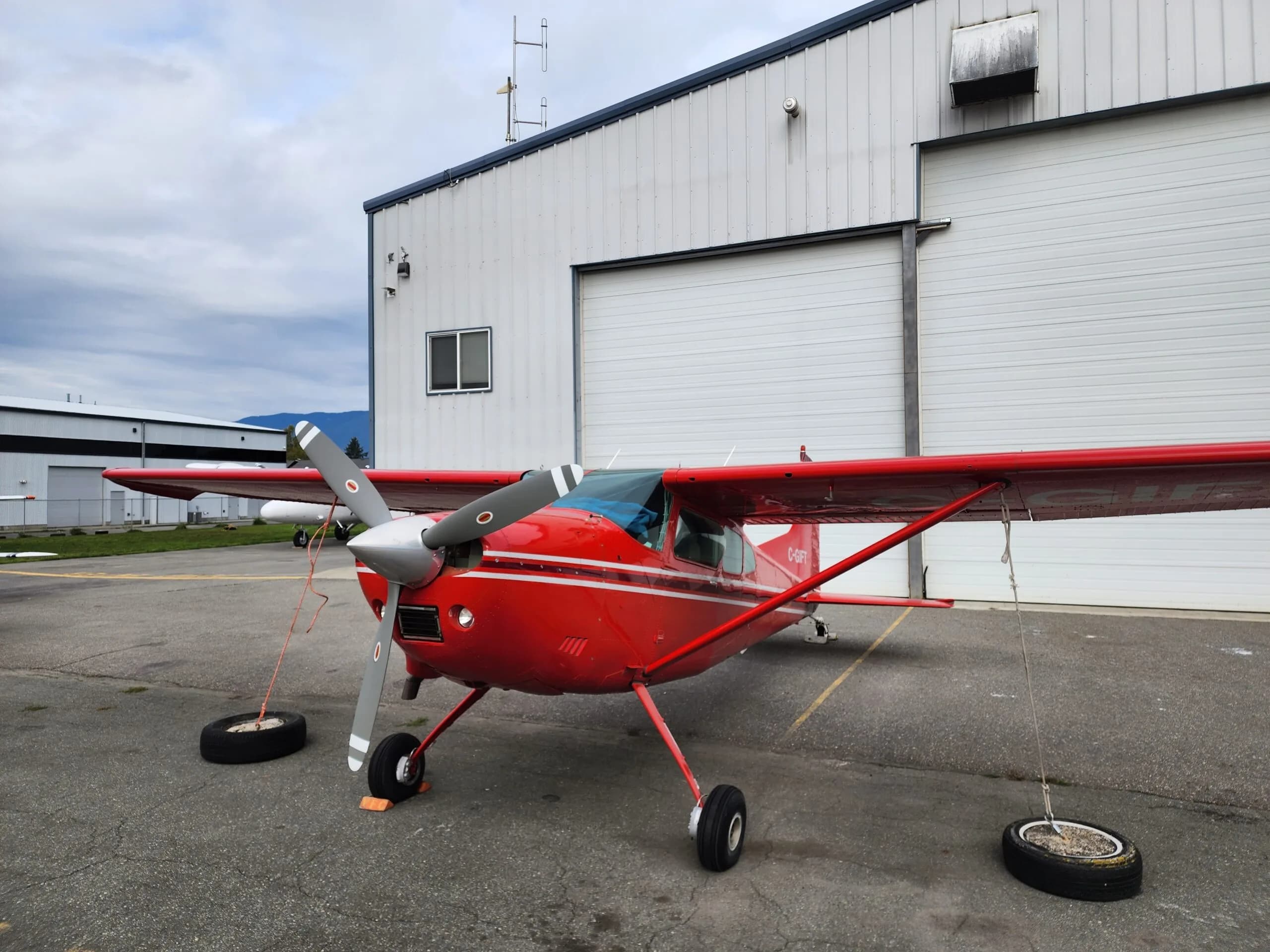 Front view of a red and white Cessna aircraft parked in front of a hangar.