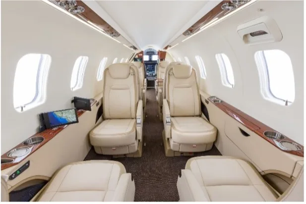 The interior of a jet with beige leather seats and wood trim.