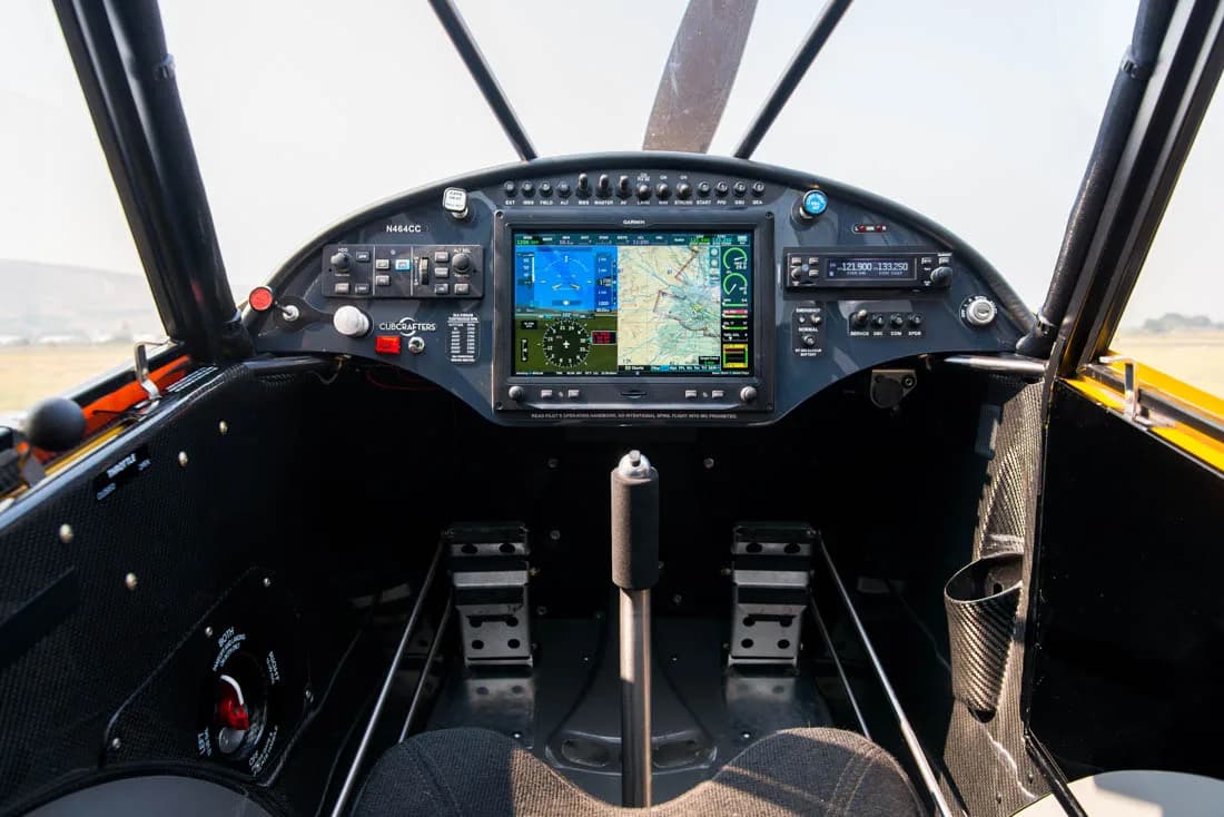 The cockpit of a Carbon Cub aircraft features a modern glass panel with two large Garmin displays and traditional controls.
