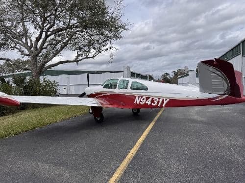 A Beechcraft Bonanza with a red and white paint scheme is parked on the tarmac.