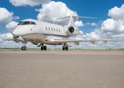A white Bombardier Challenger aircraft is parked on the tarmac under a blue sky.