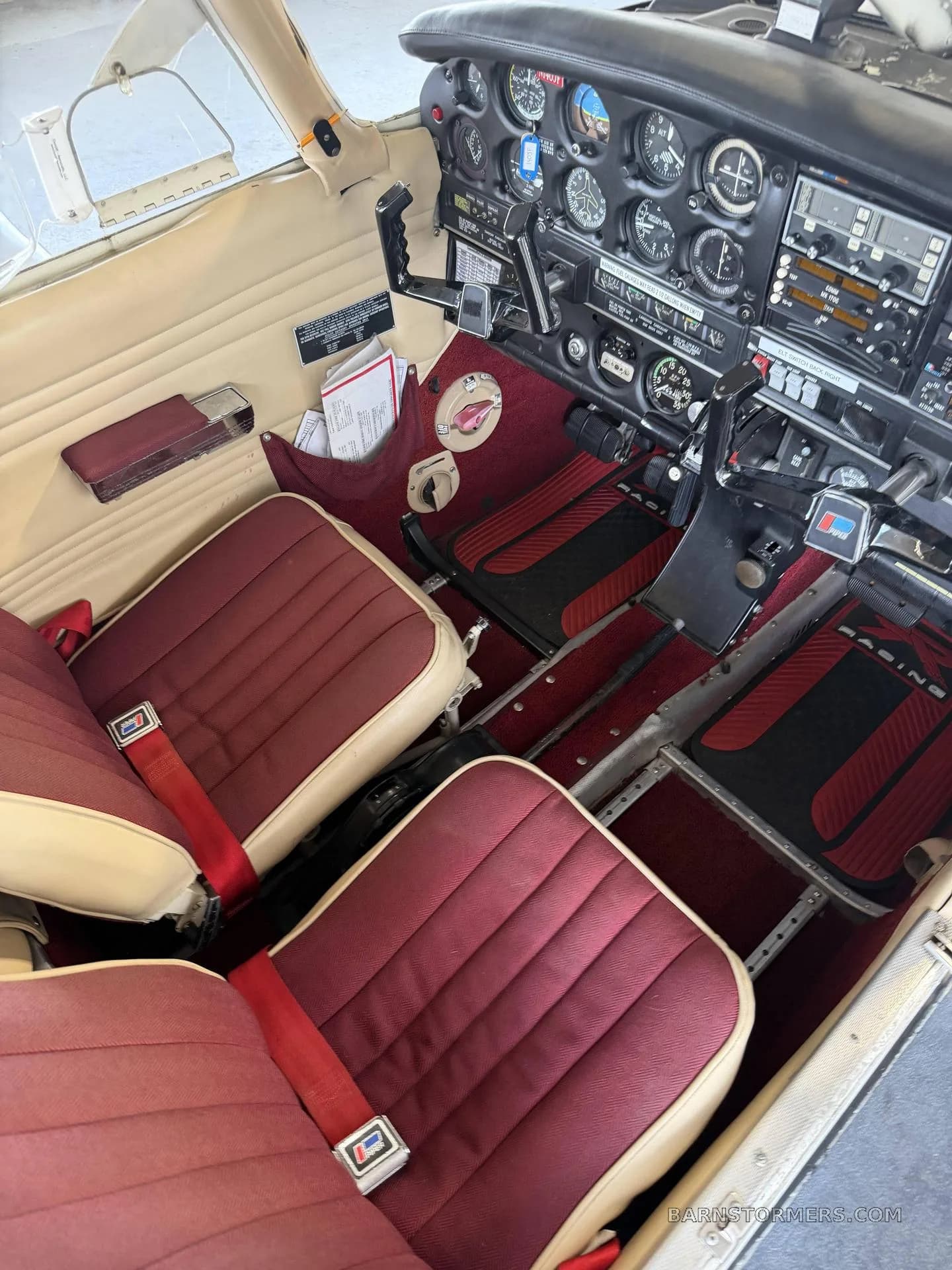 The cockpit of a small aircraft with red seats and carpet, showing the instrument panel and controls.
