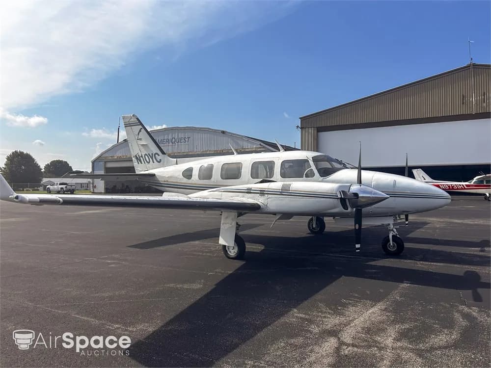 A white Piper Navajo aircraft with blue and gold stripes, registration N10YC, parked on an asphalt tarmac, viewed from the front-left.