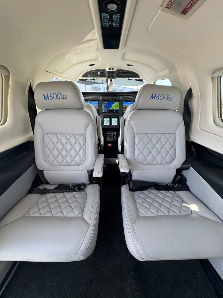The light gray leather passenger seats with "M600SLS" embroidered on the headrests, facing the cockpit.