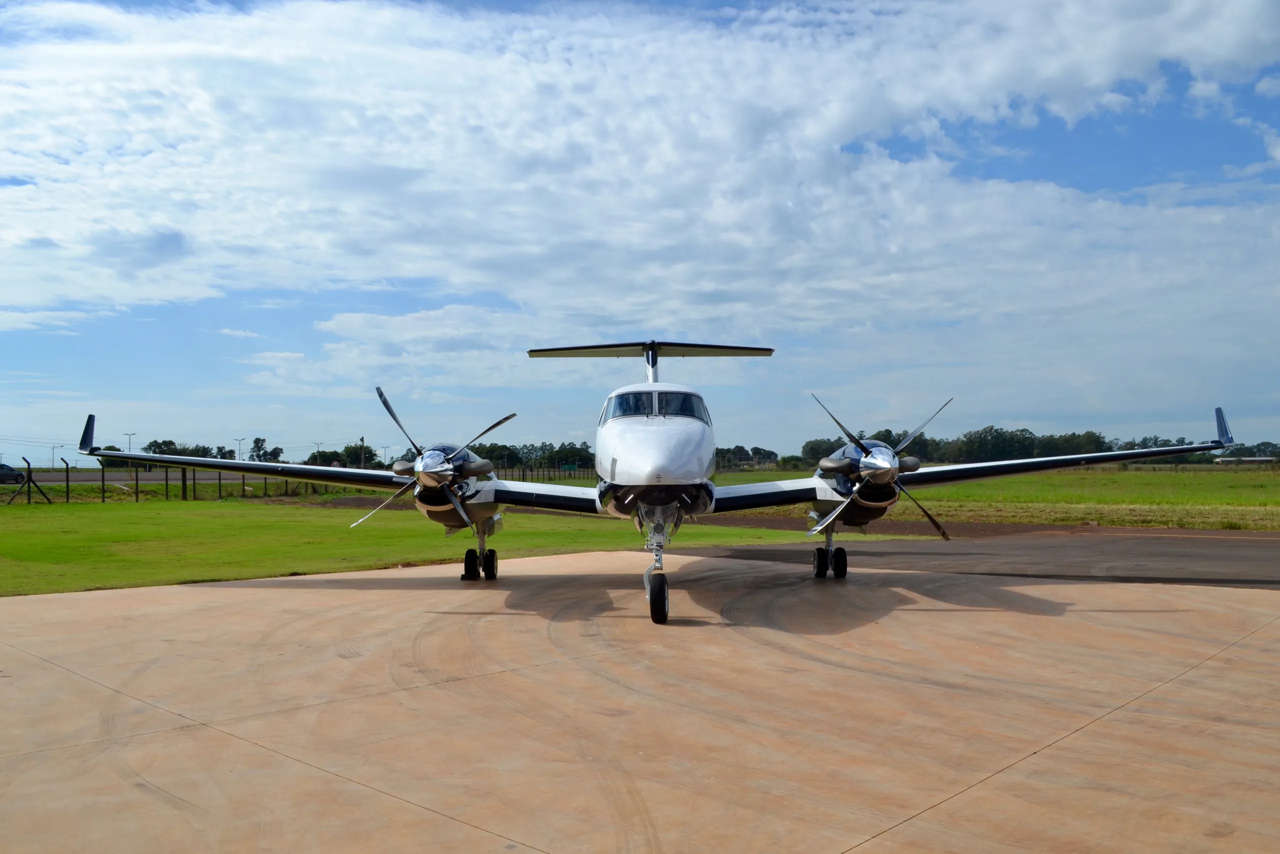 A head-on view of a white and blue twin-turboprop aircraft with its propellers and landing gear visible, on a tarmac.