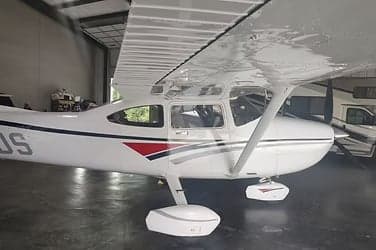 A Cessna aircraft with white and red paint scheme inside a hangar.