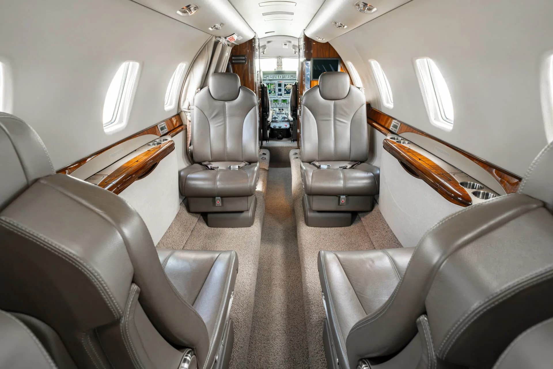 The interior of a business jet cabin looking forward towards the cockpit, showing tan leather seats.