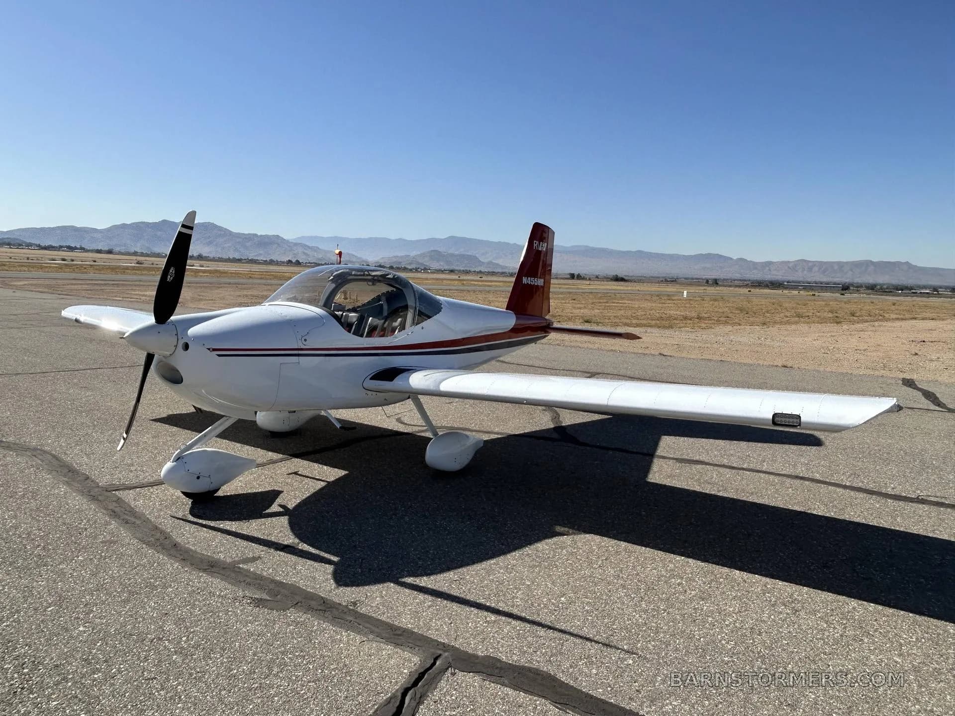 A white and red Van's RV-7 aircraft, registration N455HR, is parked on an asphalt tarmac with distant mountains, viewed from the front-right side.