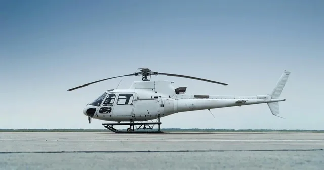 Side view of a white helicopter with skids parked on an airfield.