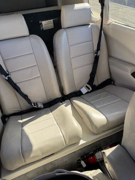 View of the aircraft's rear two light-colored leather seats with black seatbelts.