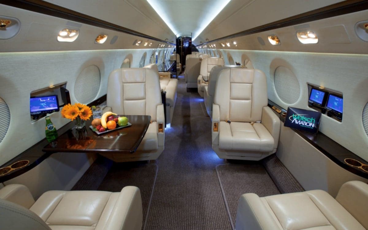 View of the aircraft interior with leather seats, a table, and monitors.