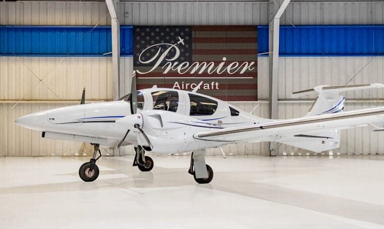 A Diamond DA62 aircraft is parked in a hangar with a Premier Aircraft banner in the background.