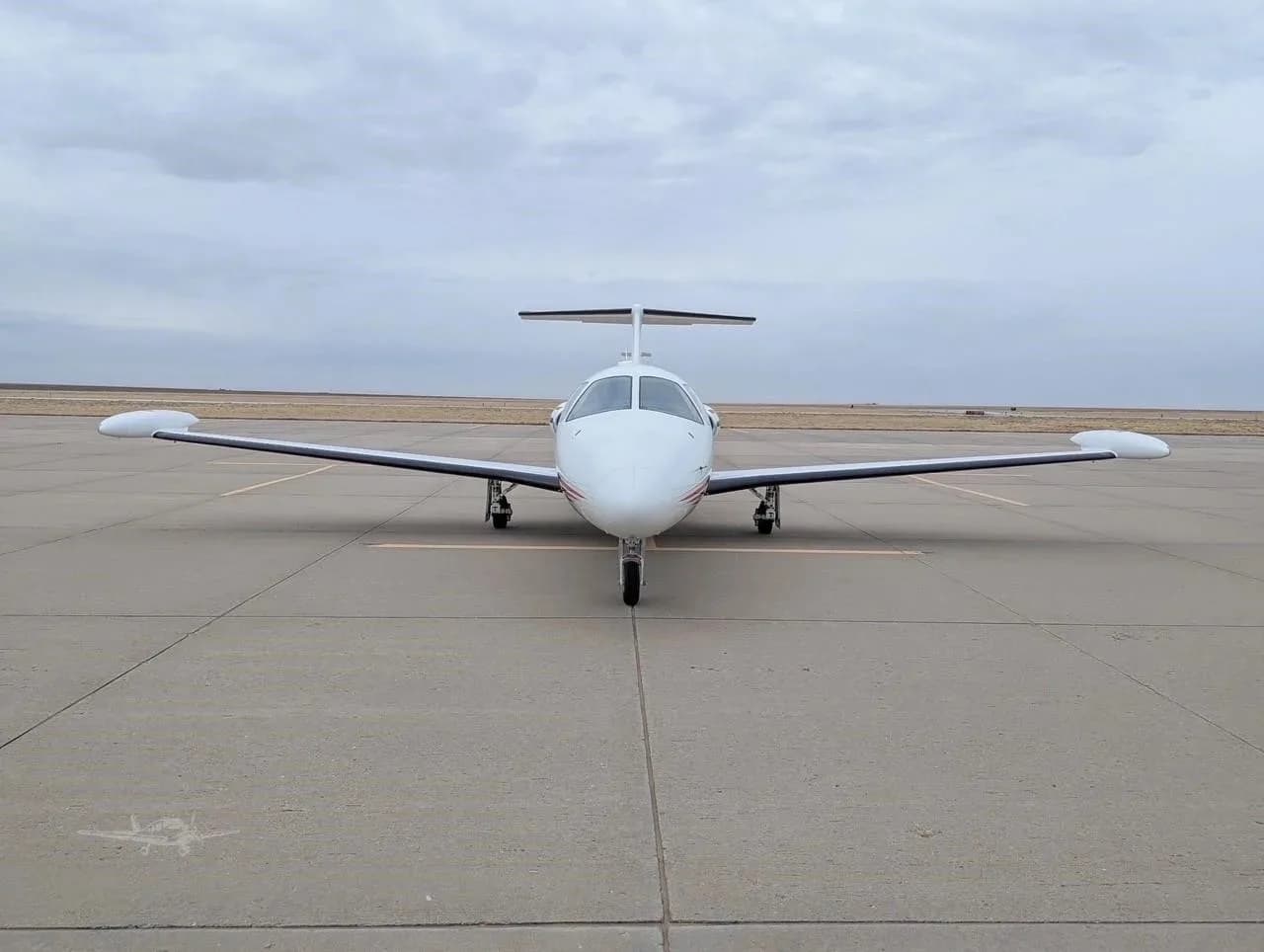 A white Eclipse jet with red and blue stripes parked head-on on an airfield under a cloudy sky.