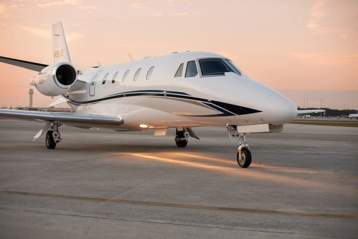 A Cessna Citation business jet on the tarmac with a white paint scheme at sunset.