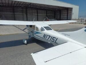 A Cessna aircraft with white paint scheme, parked on the tarmac with the tail number N1715L visible.